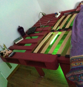 Double bed made of pallets and timber beams, neon illumination